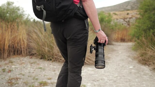 Male photographer is walking with his camera in his hand on natural trail.