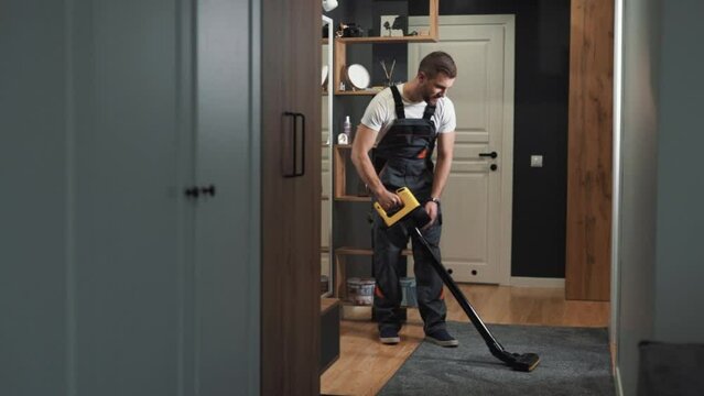 A male professional cleaner cleans a carpet with a cordless vacuum cleaner