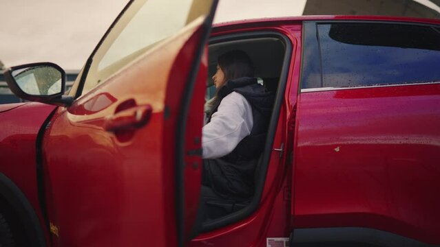 Woman with an electirc vehicle by charging station. closing door