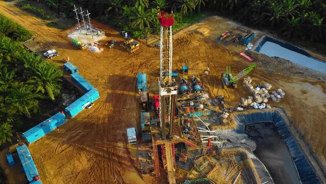 Cinematic 4K Drone Footage of Onshore Drilling Rig equipment structure for oil exploration and exploitation in the middle of jungle surrounded by palm oil trees during sunset and high oil price.