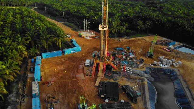 Cinematic 4K Drone Footage of Onshore Drilling Rig equipment structure for oil exploration and exploitation in the middle of jungle surrounded by palm oil trees during sunset and high oil price.