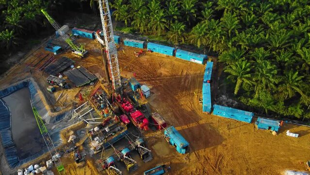 Cinematic 4K Drone Footage of Onshore Drilling Rig equipment structure for oil exploration and exploitation in the middle of jungle surrounded by palm oil trees during sunset and high oil price.