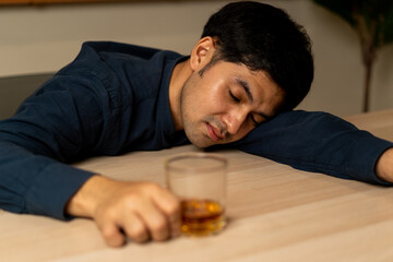 Alcoholism, depressed asian young man sleep on table while drinking alcoholic beverage, holding glass of whiskey alone at night. Treatment of alcohol addiction, suffer abuse problem alcoholism concept