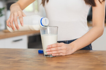 Asian slim young  woman, girl pouring of fresh, dairy milk from bottle into glass or cup, drinking and eating breakfast in morning at kitchen home. Calcium, protein for healthy lifestyle people.