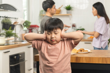 Little asian sad boy, unhappy while parents fighting, kid son not listen to shouting noise while mom and dad arguing, quarrel behind. Family suffering, stressed. Violence and divorce couple concept.