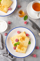 Traditional thin pancakes or crepes with cottage cheese, honey, sour cream and raspberries with cup of tea on a gray concrete background. Food for Maslenitsa. Copy space