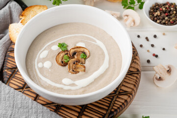 Mushroom cream soup with cream, croutons and herbs on a white wooden background. Delicious comfort food.
