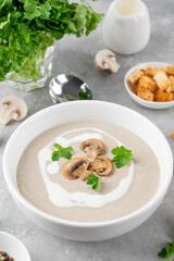 Mushroom cream soup with cream, croutons and herbs on a white wooden background. Delicious comfort food.