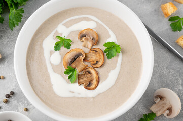 Mushroom cream soup with cream, croutons and herbs on a white wooden background. Delicious comfort food.