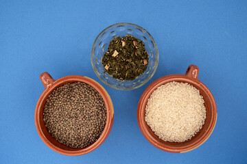 closeup overhead shot of clay and glass containers containing edible legumes and cereals on a blue background
