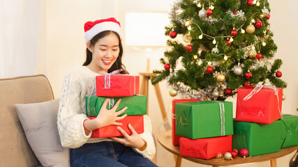 Obraz na płótnie Canvas Christmas celebration concept, Young asian woman sitting on the couch and holding christmas gifts