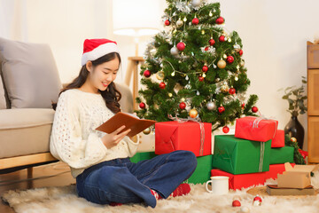 Obraz na płótnie Canvas Christmas concept, Asian woman sitting on the floor near christmas tree to writing data in notebook