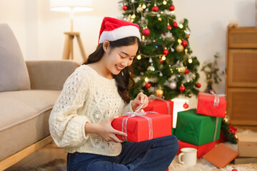 Obraz na płótnie Canvas Christmas concept, Asian woman sitting in christmas decorated living room and open christmas gift