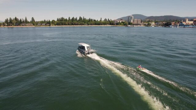 Pontoon boat pulling two kids on a tube on a lake with city in background