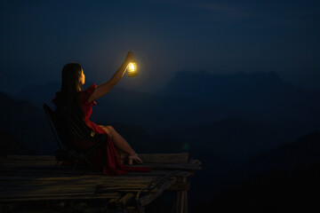 A woman sitting with a lantern in the dark night on the mountain. © Songsak C