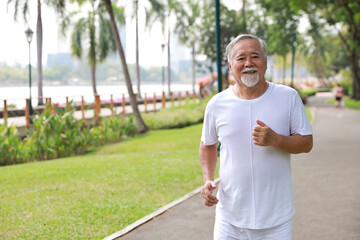 Happy and smiling asian senior man doing exercise and jogging or walking with relaxation for healthy in park outdoor after retirement during summer time. Health care elderly outdoor lifestyle concept.