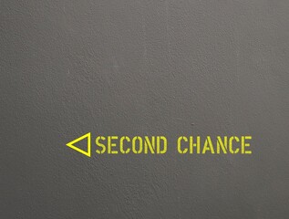 Rough gray cement wall with yellow text and direction to SECOND CHANCE, means new or more...