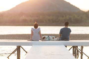 Romantic couple sitting at the beach with a dog. Happy romantic couple enjoying beautiful sunset at the beach