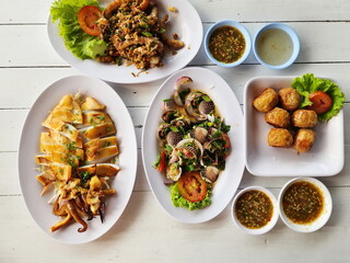 A set of spicy seafood served on a white plate includes : Grilled octopus, deep-fried crayfish with garlic, poached cockles and spicy salad, Deep fried crab meat roll (Hoi Jo) served with spicy sauce 