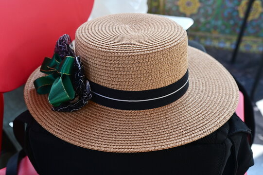 Boater straw hat with black band green bow on the side. Stylish image detail for a women's fashion. Used for wearing to protect from heat and sunlight in nature.
