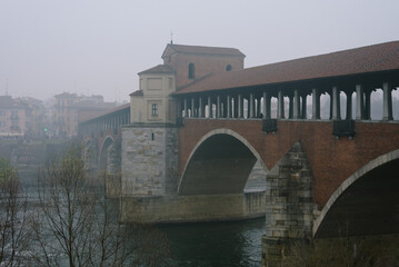 Fototapeta na wymiar Ancient covered bridge surrounded by fog in winter. Pavia. Italy