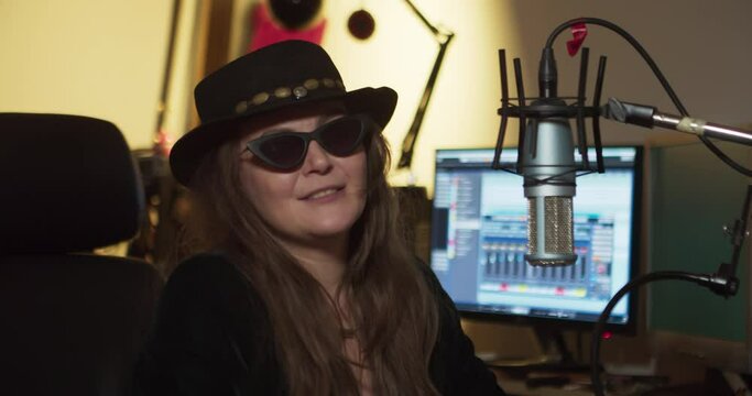 Female rocker in black glasses and a hippie hat being interviewed in a recording studio