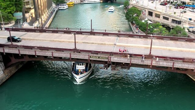 Aerial dolly out revealing touristic boat crossing under a bridge where vehicles cross in Chicago Riverwalk