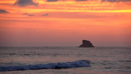 Naklejka na ściany i meble Sunset silhouetting a rocky islet at the beach in Zipolite, Mexico