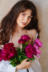 a beautiful young brunette woman in a white shirt with a bouquet of peonies.