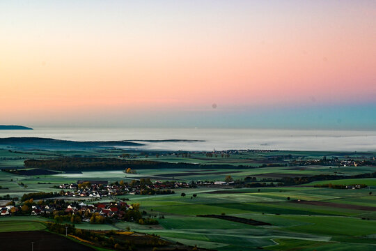 Panorama-Ausblick vom Aussichtsturm auf der Berggipfel Zabelstein bei Hundelshausen im Steigerwald, Blick &uuml;ber das Maintal nach Schweinfurt und Gerolzhofen bei Sonnenaufgang und Nebelschwaden