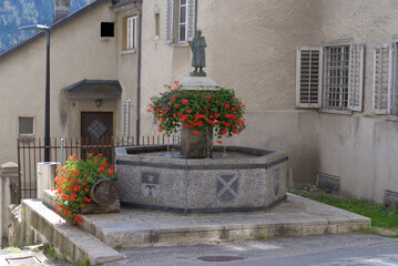 Mountain village Disentis with decorated stone fountain on a blue cloudy late summer day. Photo...