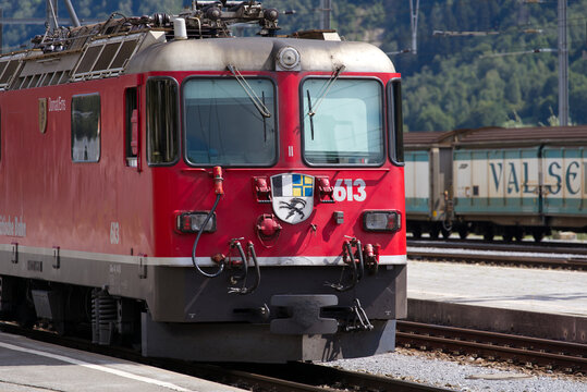 Red RHB locomotive named Domat Ems at railway station of Disentis Must&eacute;r on a sunny late summer day. Photo taken September 5th, 2022, Disentis, Switzerland.