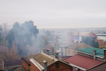 smoke from a fire or the burning of autumn foliage and debris rises above the roofs of houses. view from above.