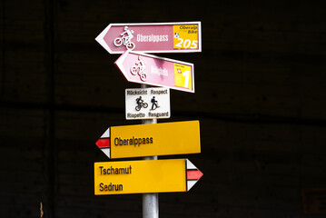 Red and white mountain bike trail sign and yellow hiking trail sign at Swiss mountain pass Oberalppass on a sunny late summer day. Photo taken September 5th, 2022, Oberalp Pass, Switzerland.