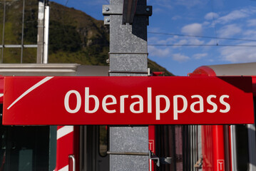 Railway station Oberalppass with sign and train at mountain panorama on a sunny late summer day. Photo taken September 5th, 2022, Oberalppass, Switzerland.