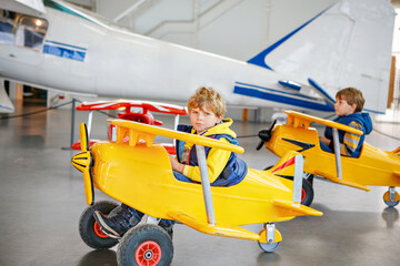 Twee kleine jongens die een groot stuk speelgoed oud vintage pedaalvliegtuig besturen en plezier hebben, binnenshuis. Actieve vrijetijdsbesteding met kinderen tijdens schoolvakanties.