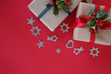 Two Christmas gifts with Holly branch with red berries and silver decorations on a red background with copy space
