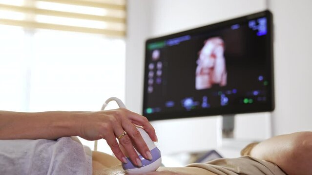 Ultrasonic check for the pregnant patient. Doctor is performing ultrasound diagnostics to a woman with big belly. Screen at backdrop in blur.