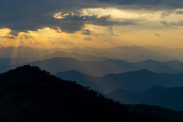  Sunset with clouds in the mountains. The sun's rays pass through the clouds late evening. Ray of the sunset with mountains and sky background. Beautiful sun beam pass through the cloud. .