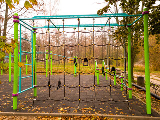 Climbing net and modern gym equipment for workout on empty sports field in a city park on a foggy autumn morning