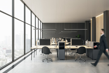 Businessman walking in modern coworking office interior with equipment, furniture and panoramic window with city view.