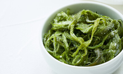 heap of fresh Korean salted seaweed salad stem side dish or Miyeok Julgi Bokkeum in white bowl on white background. Laminaria or Kelp Seaweed stem                          