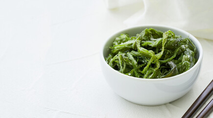 heap of fresh Korean salted seaweed salad stem side dish or Miyeok Julgi Bokkeum in white bowl on white background. Laminaria or Kelp Seaweed stem                          