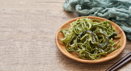 heap of fresh Korean salted seaweed salad stem side dish or Miyeok Julgi Bokkeum in wood bowl on wooden table background. Laminaria or Kelp Seaweed stem                                              © boommaval