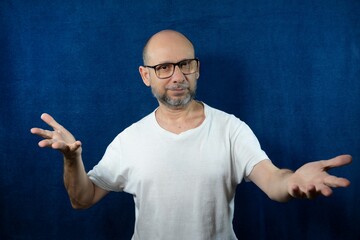 Portrait of a bearded bald man doing a gesture against the blue background