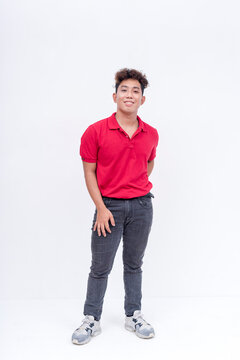 A confident filipino man with curly hair wearing a red polo shirt and blue jeans. Isolated on a white background.