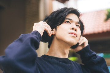 Portrait of young adult asian men with black short hair using headphone listen music at outdoor on day