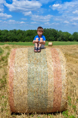 Naklejka na ściany i meble The boy is sitting on golden hay bales on the field