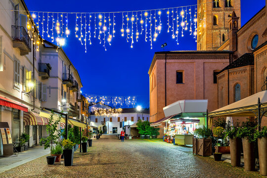 Cobblestone street in old town of Alba illuminated with Christmas lights.