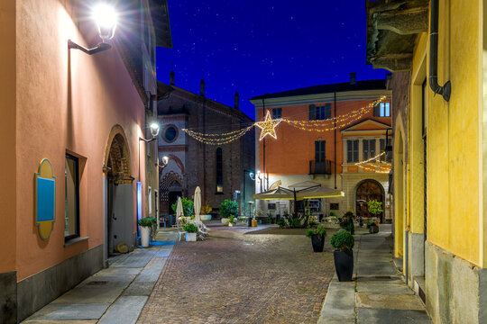 Narrow cobblestone street among old buildings and Christmas illumination in Alba, Italy.